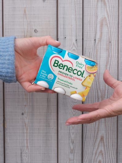 Woman's hand giving older woman's hand a pack of benecol yoghurt drinks